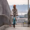 A person wearing an orange helmet and beige clothing rides a blue Soltera 2.5 Ebike on a bridge. A text overlay reads, "300 lb payload.
