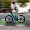 Riding the Soltera 2.5 Ebike, a helmeted cyclist in light clothing crosses a city street, the blurred background highlighting their speed and motion.