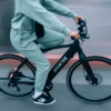 A person in a green tracksuit rides a black Soltera 2.5 Ebike on a paved road, with a blurred background capturing the sense of motion.