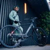 A person in green activewear and helmet stands outside, smiling and holding the handlebars of a black Soltera 2.5 Ebike.