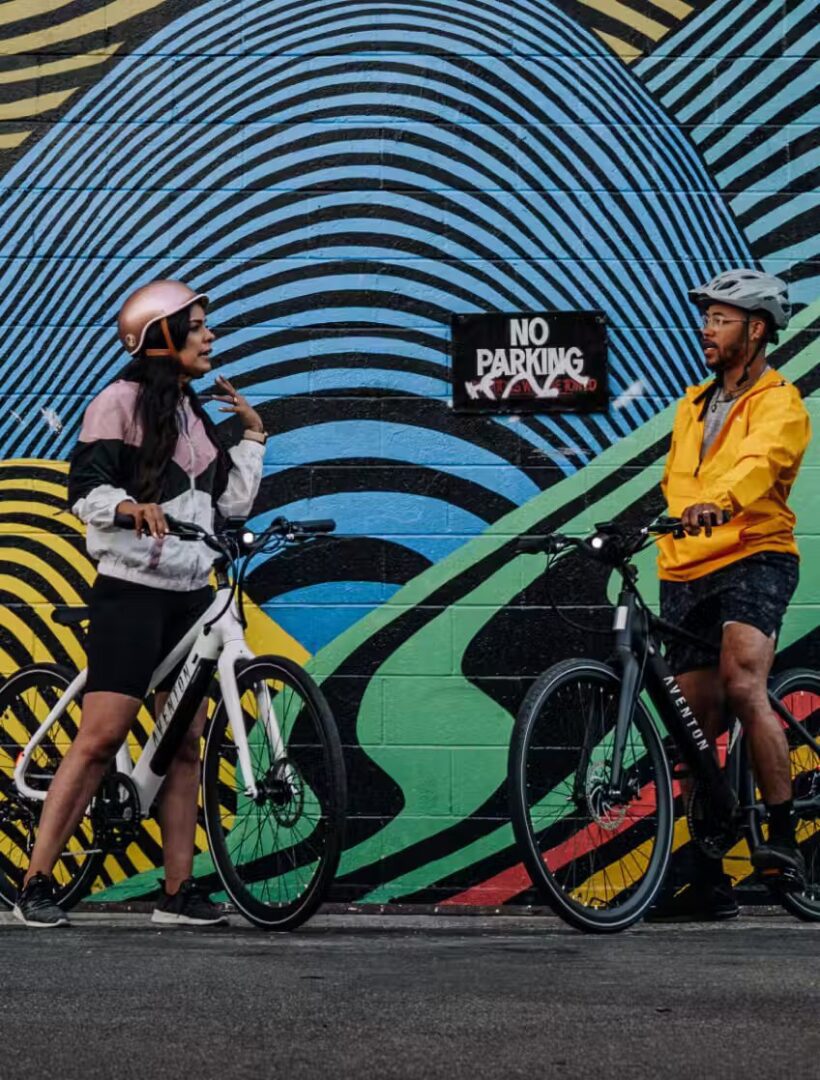 Two people standing in front of a colorful mural, showcasing e-bikes accessories.