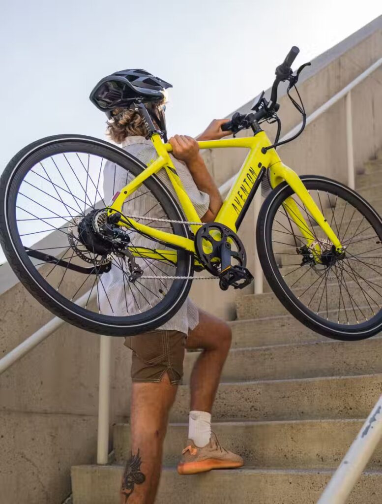 A man carrying a yellow e-bike up some stairs.