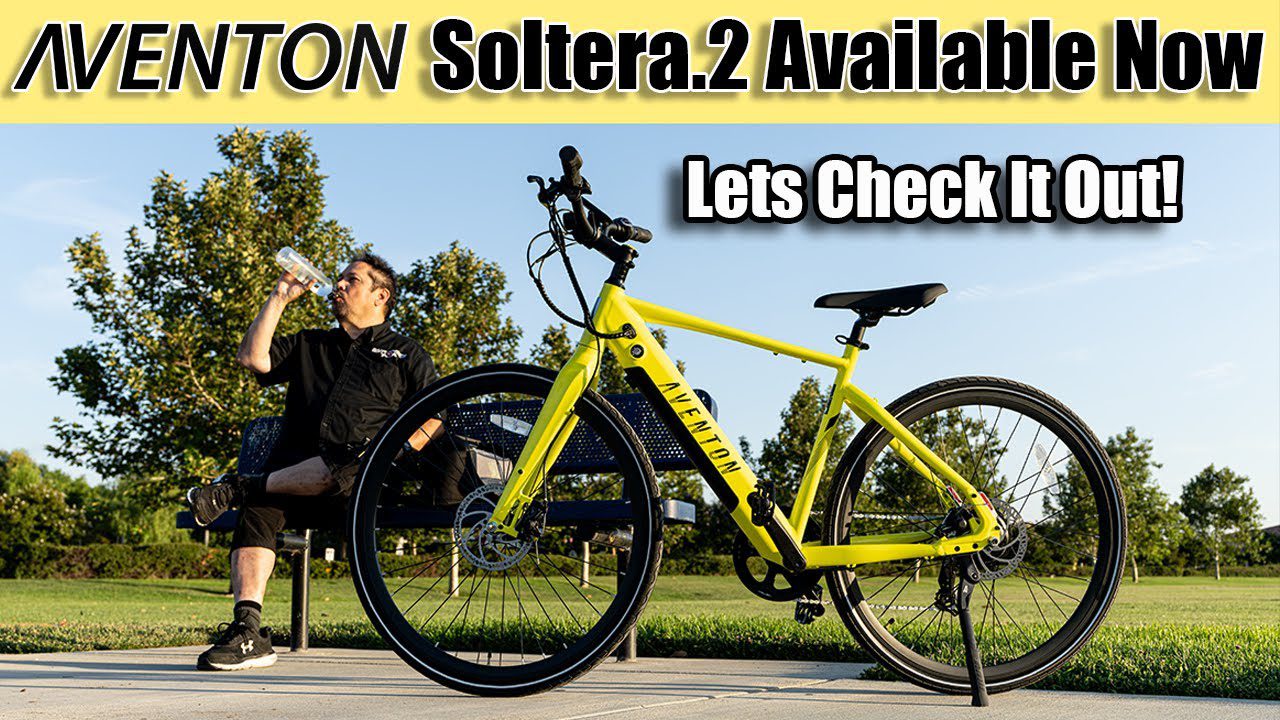 A woman is sitting on a bench next to a yellow bicycle, specifically an ebike.