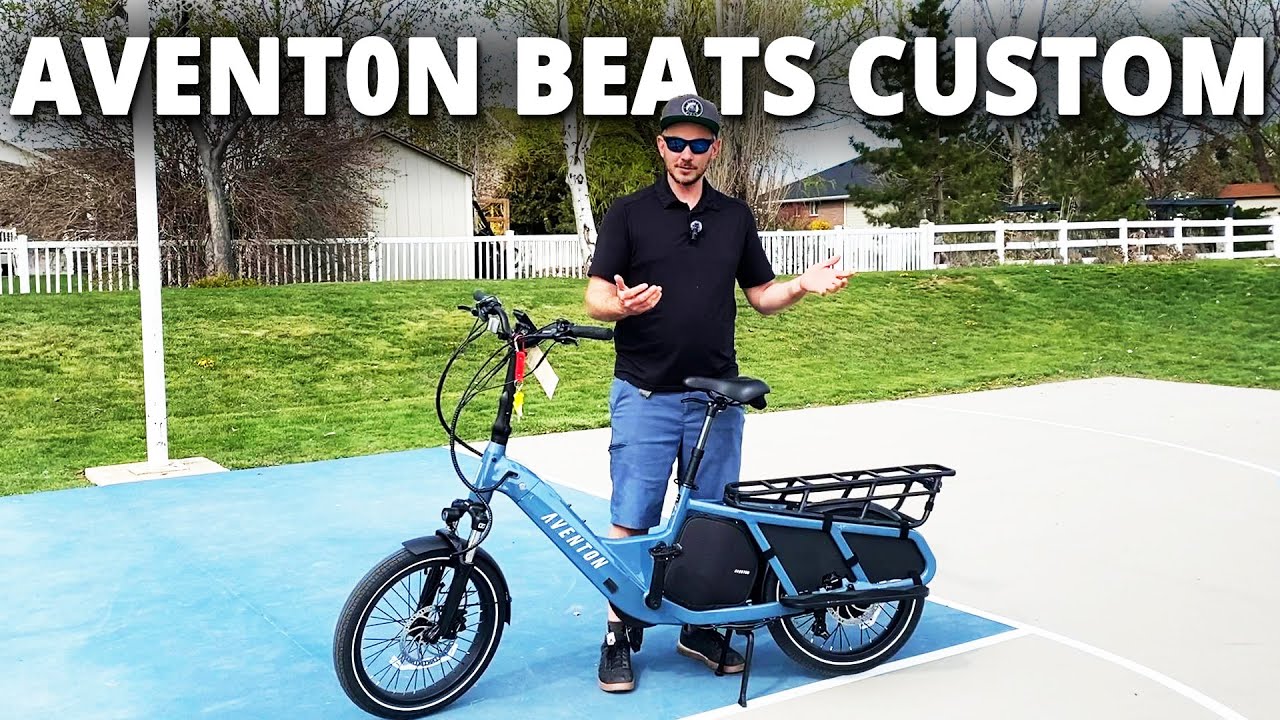 A man standing next to a blue bicycle with the words "aventon beats custom" showcasing ebikes accessories.