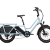 A light blue, electric cargo bike with a step-through frame, black saddle, and integrated rear cargo rack. The bike has front and rear fenders and an electric motor mounted in the rear wheel hub.