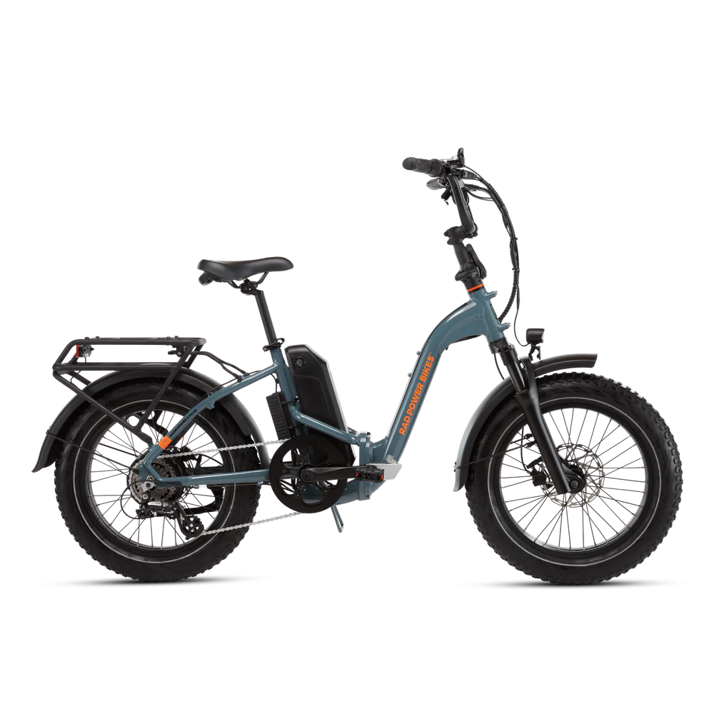 A blue electric bike with thick tires, a rear cargo rack, front suspension, and an adjustable seat stands against a plain black background.