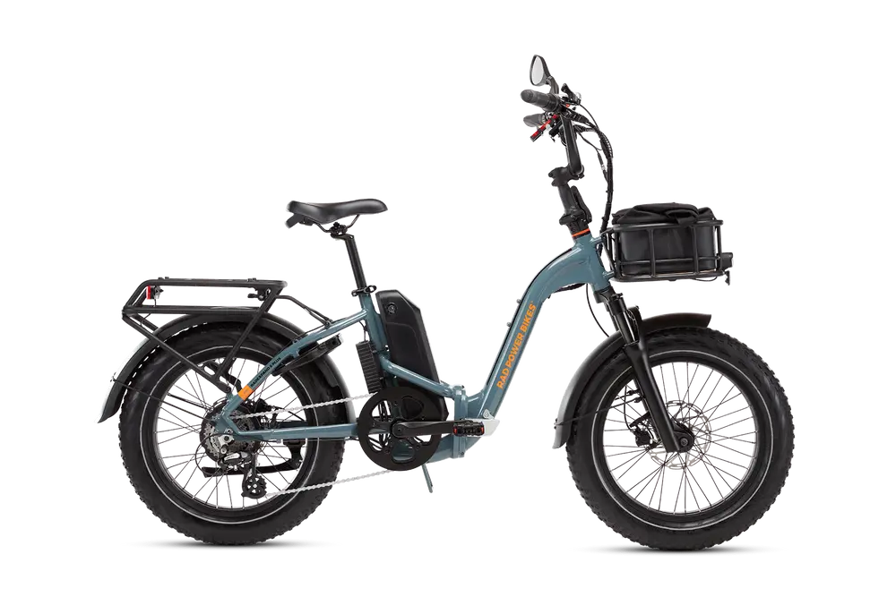 A blue electric bicycle with thick tires, a mounted battery, rear cargo rack, front basket, and black seat. The bike has a low frame and is designed for multiple terrains.