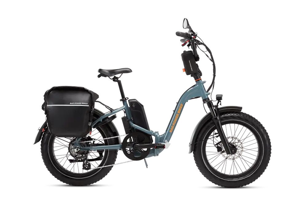 A blue electric bicycle with a rear black pannier bag, a step-through frame, and thick tires on a white background.