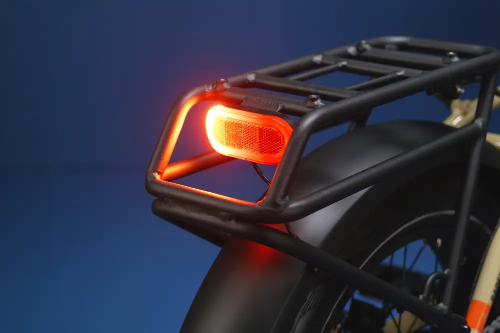 Close-up of an illuminated rear light on a black bicycle rack with a dark blue background.