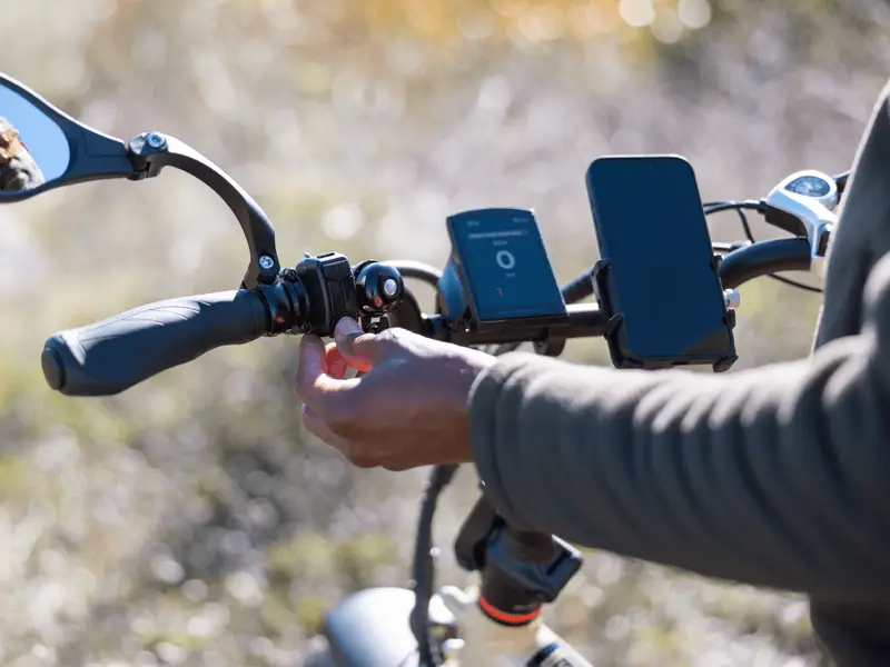 Close-up of a person adjusting the handlebar of a bicycle with a smartphone and a speedometer mounted on it.