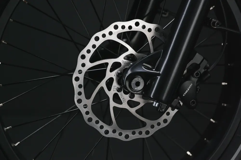 Close-up of a bicycle's disc brake mechanism. The image shows the brake rotor attached to the wheel and the caliper mounted on the fork, all against a dark background.