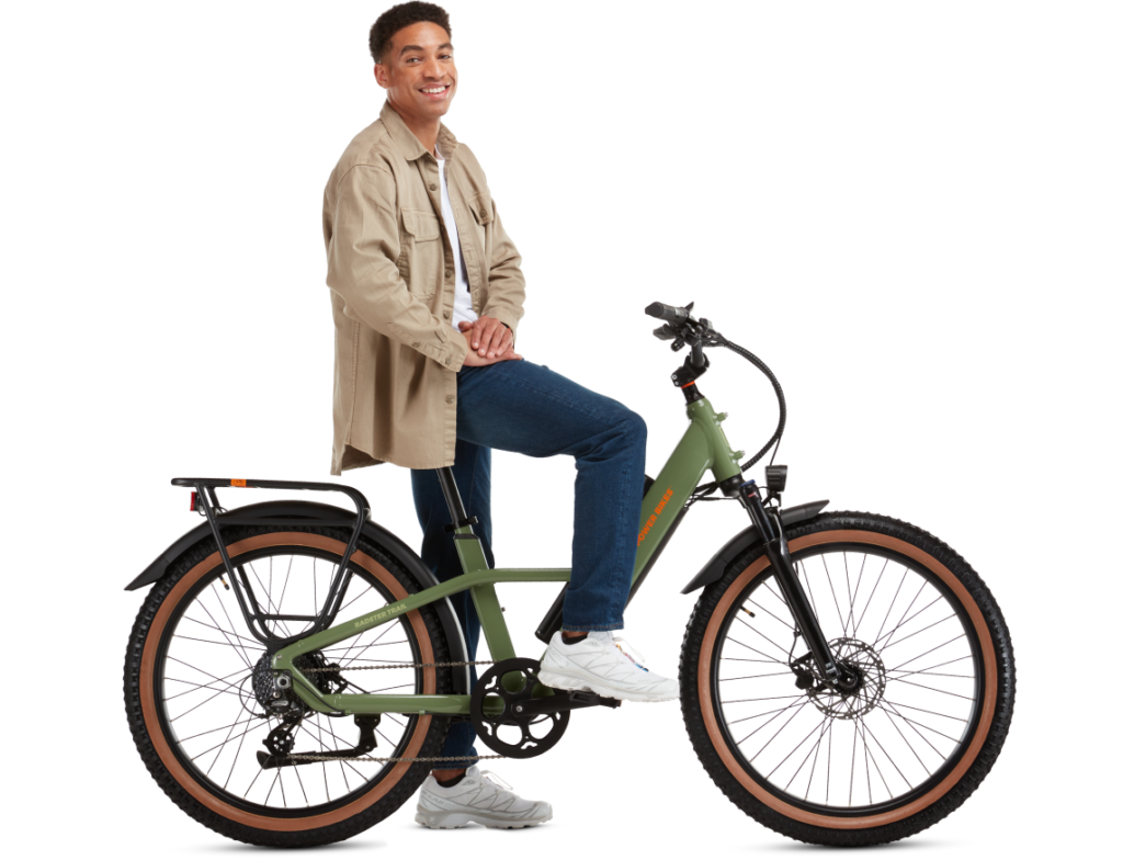 A man in casual clothing smiles while sitting on a green electric bicycle. The bike has thick tires, a rear rack, and orange accents.