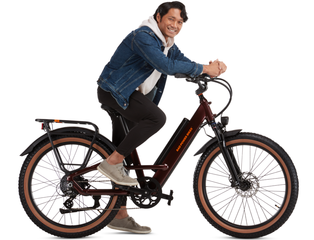 A person in a denim jacket and black pants sits smiling on an electric bike, ready to ride.