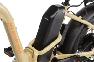 Close-up of a Rad Power Bikes electric bicycle frame showing a mounted battery pack. The bike is beige with "Rad Power Bikes" text on the frame.