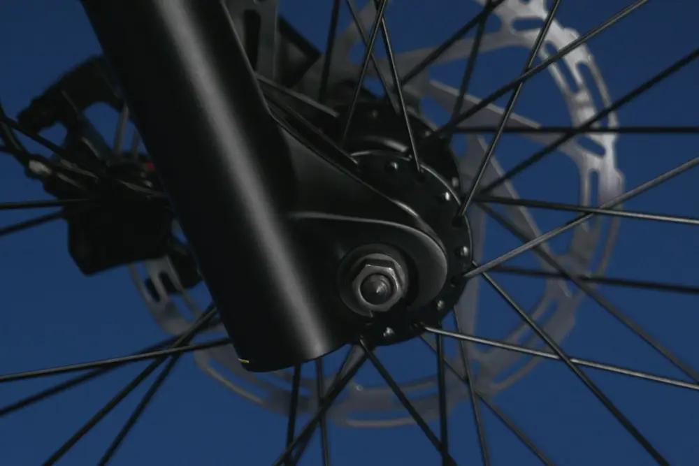 Close-up image of a bicycle wheel hub with visible spokes and brake disc against a blue background.