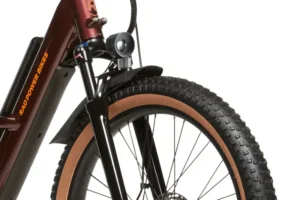 Close-up of the front section of a bicycle with a brown frame and the text "Rad Power Bikes" on it. The image shows the front wheel, tire, fender, and part of the suspension fork.