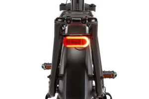 Rear view of a bicycle with a lit red tail light and black frame, showcasing its rear wheel, pedals, and rack.