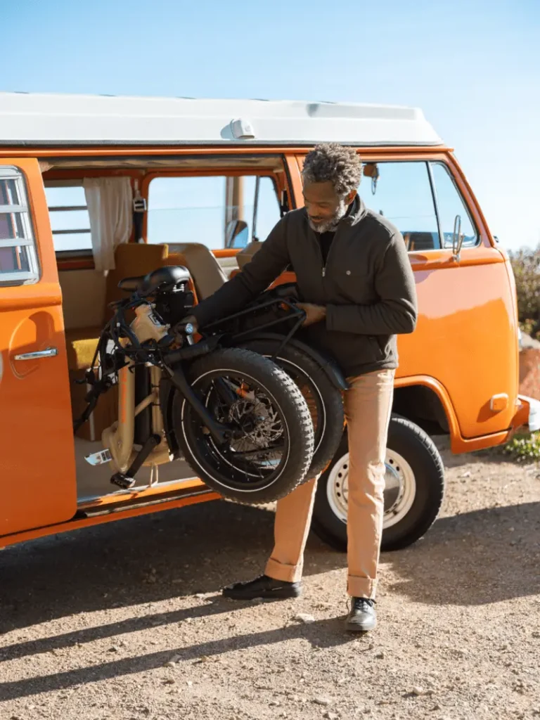 A man lifts a folded bicycle from an orange van on a sunny day.