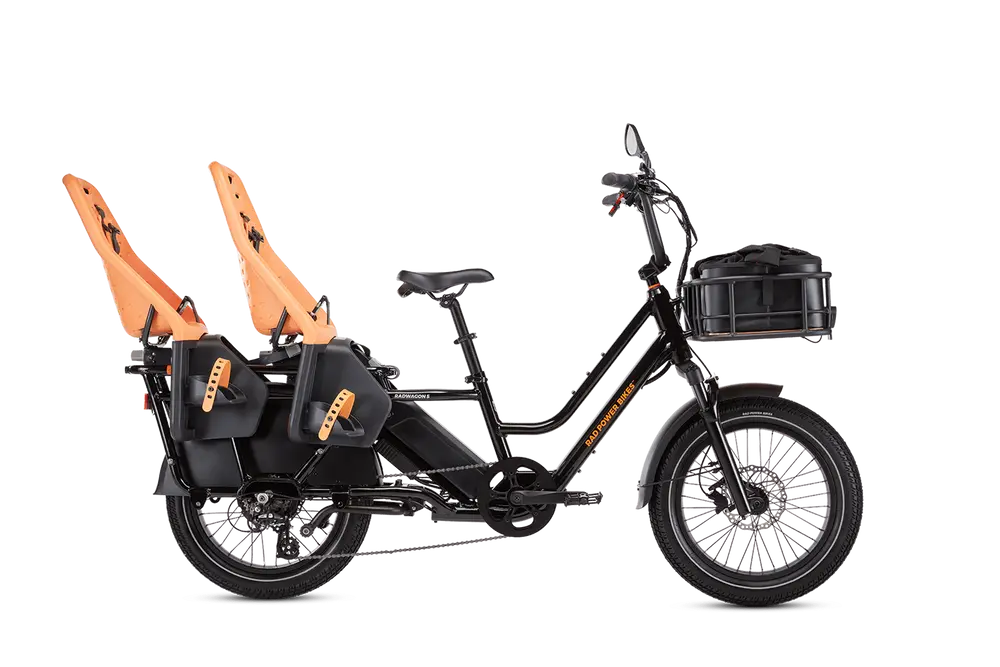 A black electric cargo bike with orange child seats mounted at the rear and a large storage basket at the front.