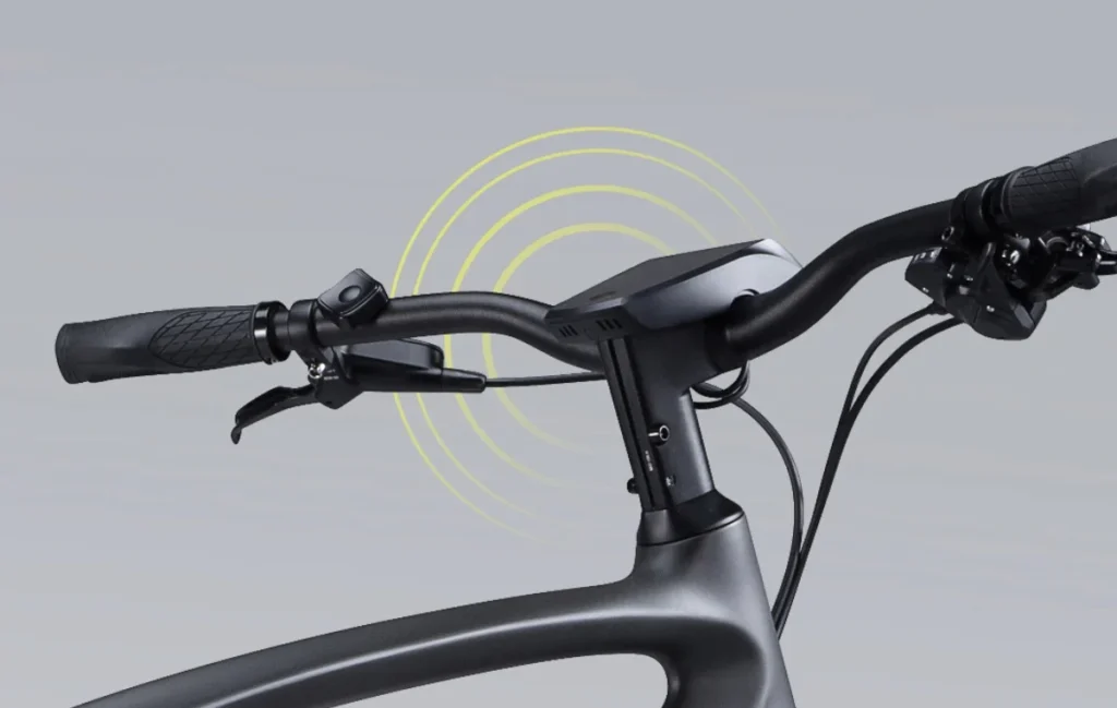 Close-up of a bicycle's handlebars and display screen with yellow concentric circles emanating from the screen, indicating connectivity or a signal. Black grips and brake levers are visible.