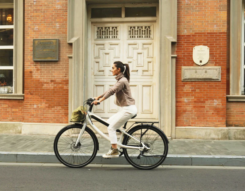 A person rides a bicycle on a street with brick buildings in the background.