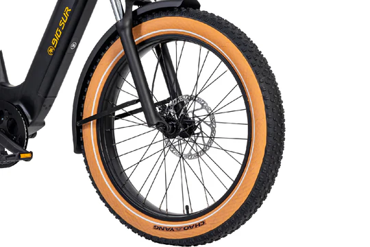 Close-up of the front wheel of a bicycle with a black fork, disc brake, and tire with a beige sidewall. The word "CHAOVANG" is printed on the side of the tire. A small part of the bike frame is visible.