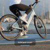 Cyclist riding an electric bike by a marina, with mountains in the background. Text overlay: "750W peak power.