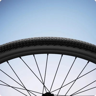 Bicycle wheel with a textured tire and spokes against a clear blue sky background.