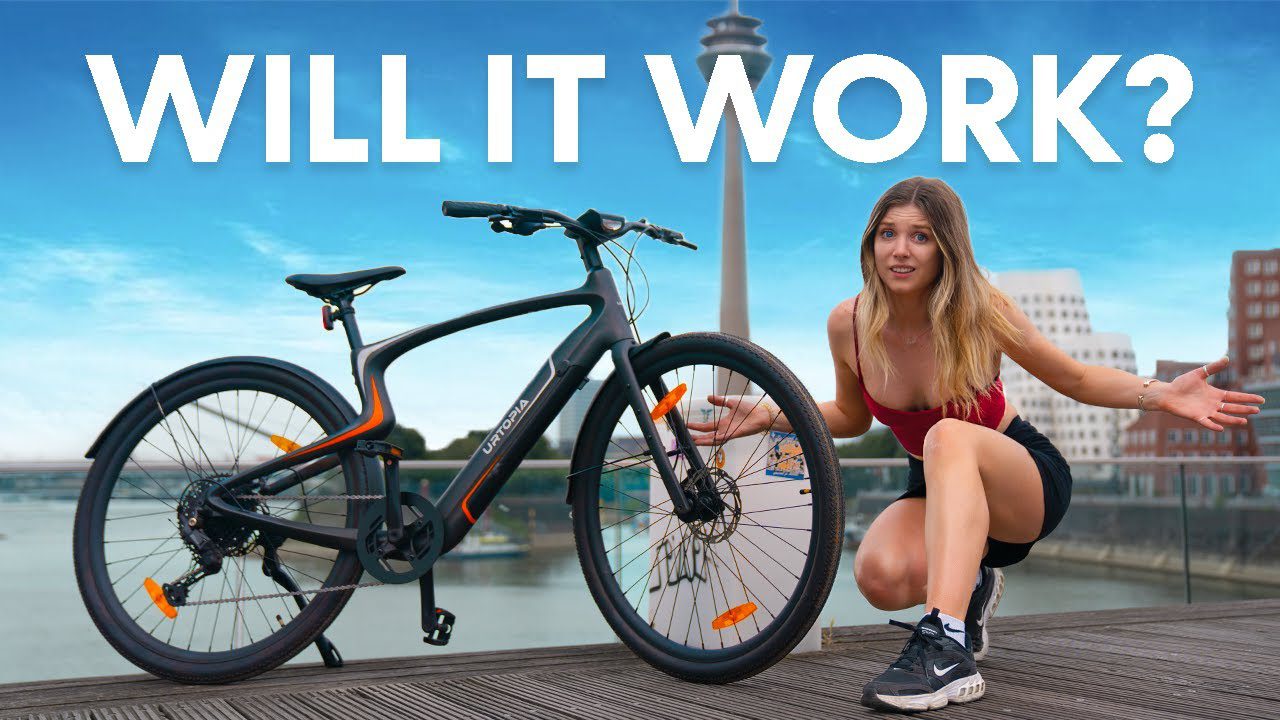 A woman kneels beside an electric bike on a wooden platform with the city skyline in the background. Text above reads, "Will it work?.