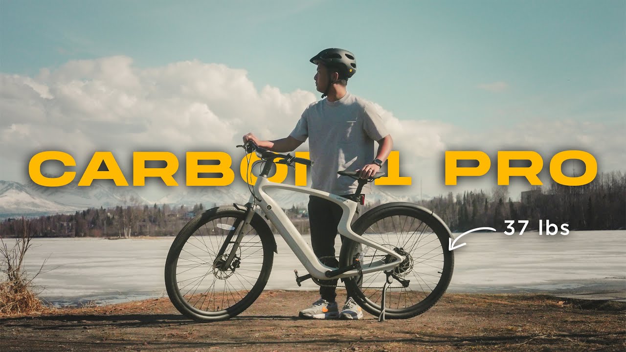 Person wearing a helmet stands with a Carbon 1 Pro bike beside a lake, labeled "37 lbs," with snowy mountains in the background.