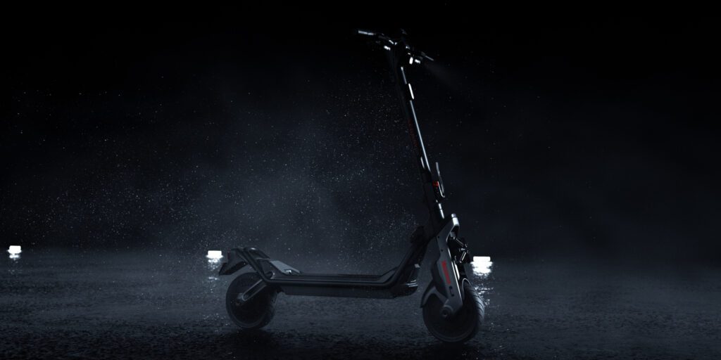 A black electric scooter stands on a wet surface with a dark background and a misty atmosphere, illuminated by minimal white lights.