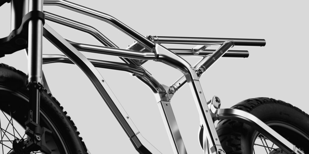 Close-up of a metallic bicycle frame with large tires, showing the structure and tubing against a neutral background.