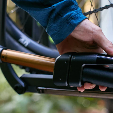 Close-up of a person’s hand unlocking or adjusting a bike frame near the rear wheel, with a focus on the locking mechanism and the chain.