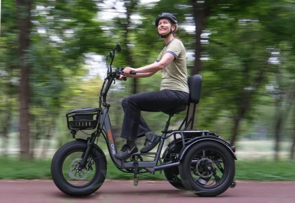Wearing a helmet, a person rides the Meet One Breeze Folding Electric Trike along a path in a lush, tree-filled park.