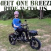An older adult in a pink helmet sits on the Meet One Breeze Folding Electric Trike outdoors on grass with trees behind, and "Meet Our E-Biker" text above.