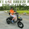 A person in an orange shirt and helmet sits on a paved road lined with trees atop the Meet One Breeze Pro Fat Tire Electric Trike, with "Meet the Breeze Pro Ride With Us" above.