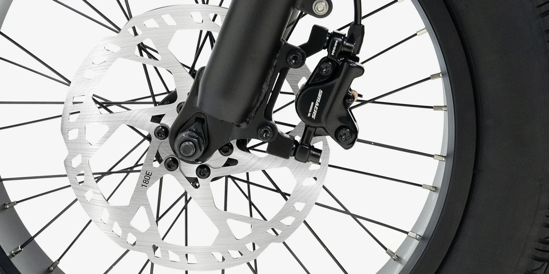 Close-up view of a bicycle front wheel featuring a disc brake rotor, caliper, and spokes against a white background.