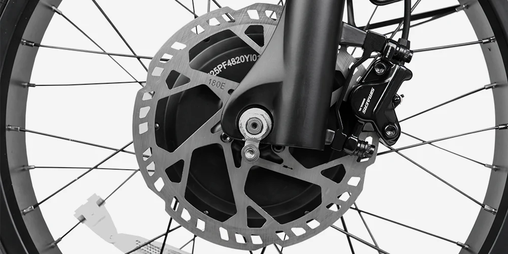 Close-up of a bicycle wheel showing a disc brake rotor, brake caliper, and spokes attached to the hub and fork.
