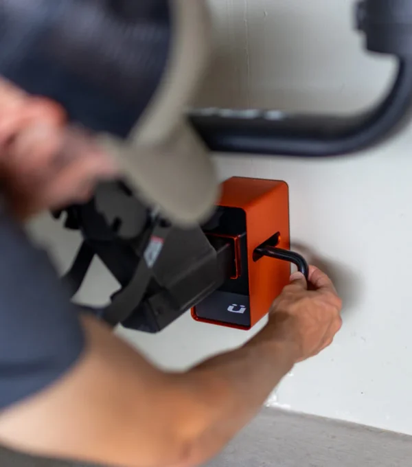 Someone uses a key to lock or unlock the Rack Dock, a wall-mounted box, while holding a large item in their other hand near the device.