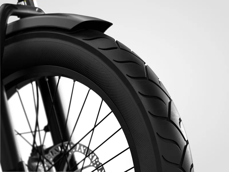 Close-up view of a black bicycle tire with a tread pattern, metal spokes, and a disc brake against a plain background.