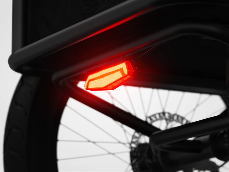 Close-up of a red rear LED light mounted on the frame of a bicycle, with part of the wheel and disc brake visible in the background.