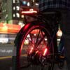 A person stands next to a Tarmac ST Ebike, its smart tail light shining brightly at night against a backdrop of blurred city lights and buildings.