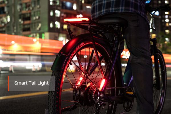 A person stands next to a Tarmac ST Ebike, its smart tail light shining brightly at night against a backdrop of blurred city lights and buildings.
