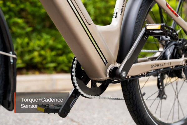 Close-up of the Asphalt Ebike’s pedal and chain area labeled "Torque+Cadence Sensor," with parts of the frame and rear wheel visible.