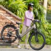 A woman in a helmet and sunglasses stands outdoors holding an Asphalt Ebike, with a sign near the bike that reads "Lightweight Frame.