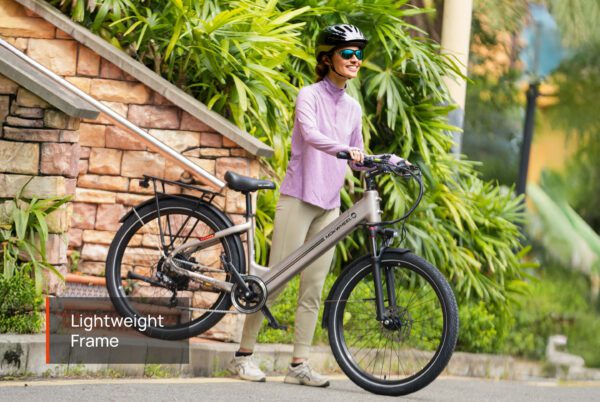 A woman in a helmet and sunglasses stands outdoors holding an Asphalt Ebike, with a sign near the bike that reads "Lightweight Frame.