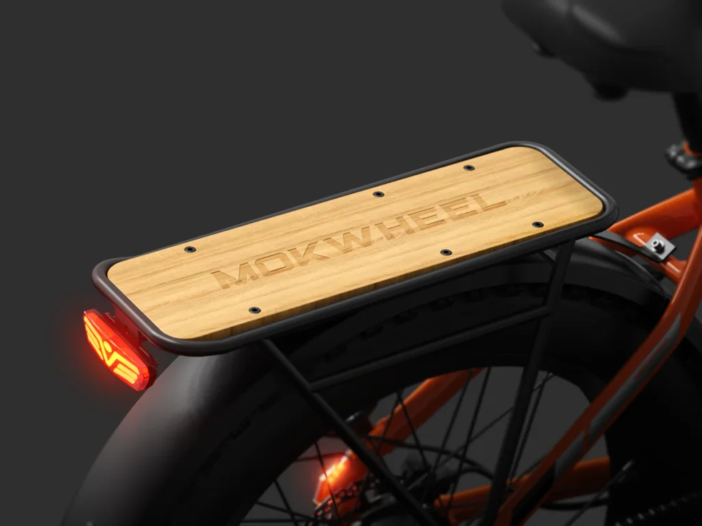 A wooden rear rack with "MOKWHEEL" engraved, mounted on the back of an orange bicycle above a black tire, next to a red rear light.