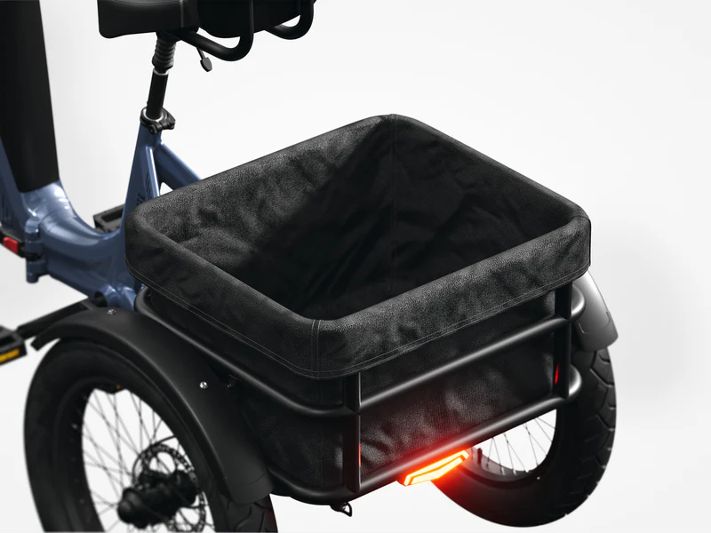 Close-up of a black fabric cargo basket mounted on the rear of a blue bicycle, with a red rear light visible below the basket.