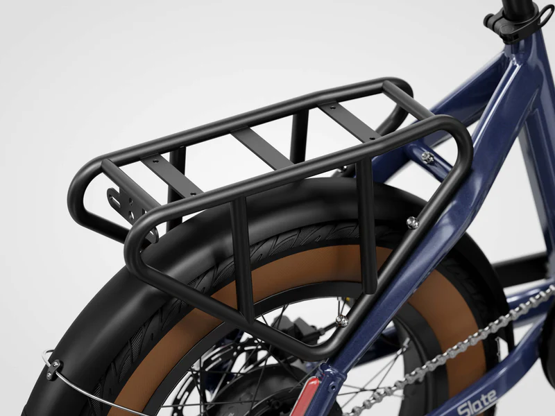 Close-up of a black rear cargo rack mounted above the back wheel of a blue bicycle, showing part of the tire, fender, and bike frame.