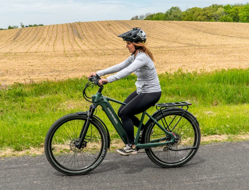 A person wearing a helmet and athletic clothing rides an electric bicycle on a paved road beside a field.